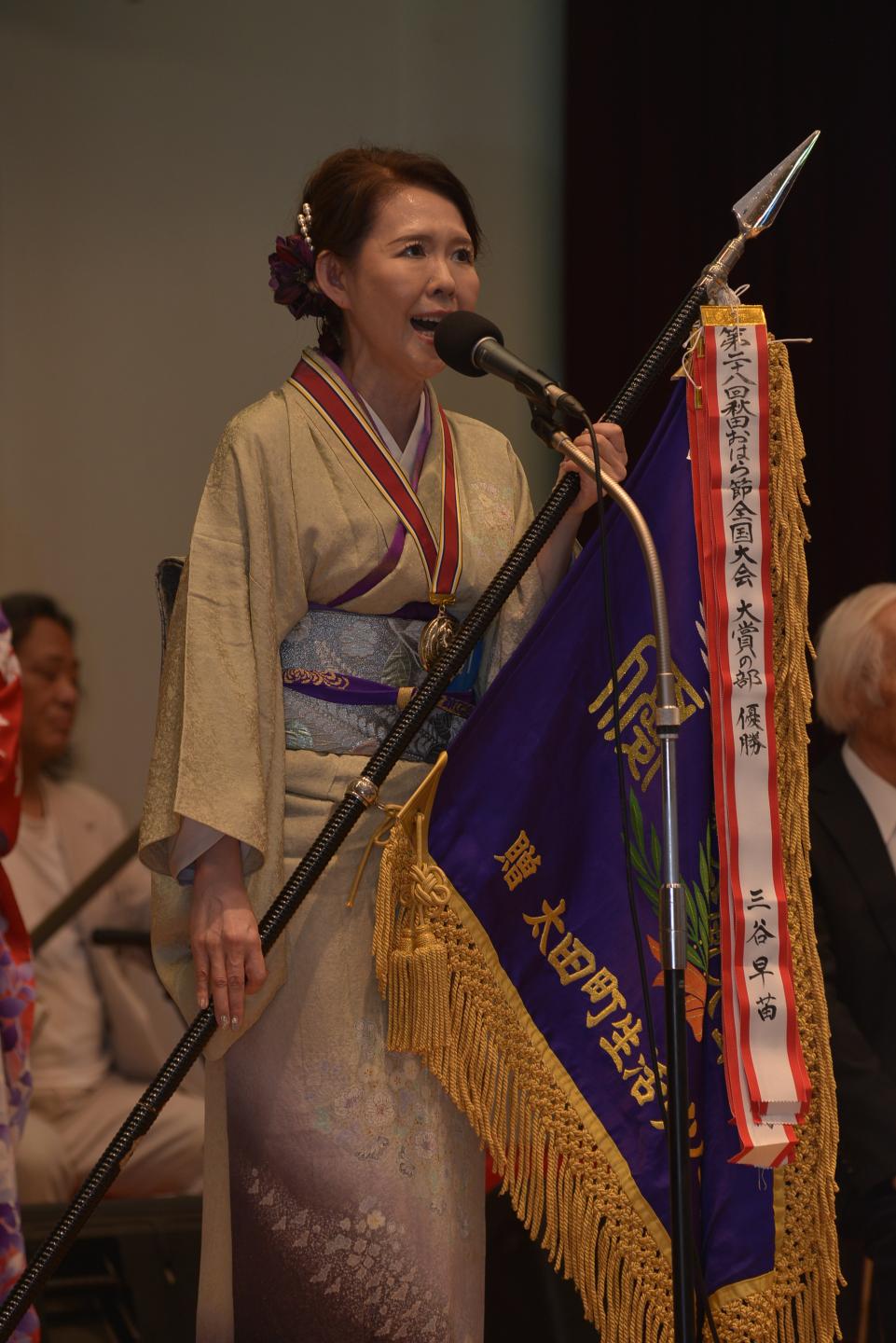 大賞の部優勝の三谷さん、優勝旗を持って歌唱している